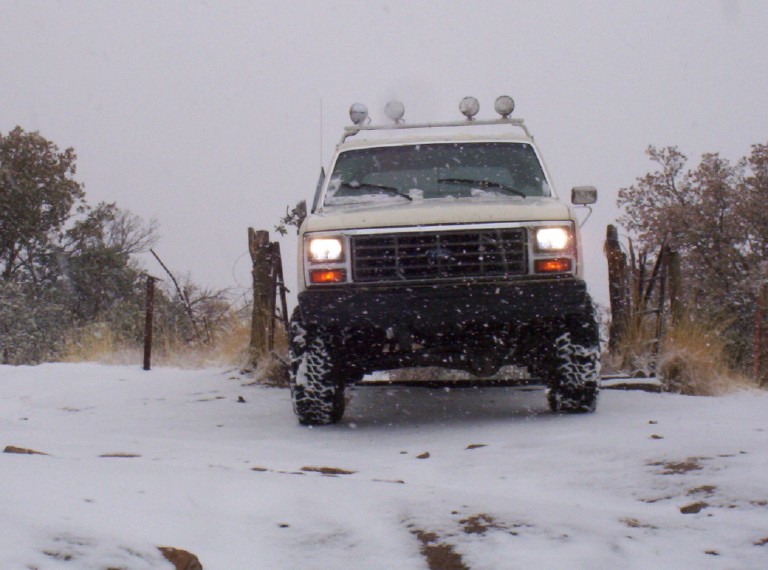 White SUV with off-road lights on roof driving in snow. Front grille visible