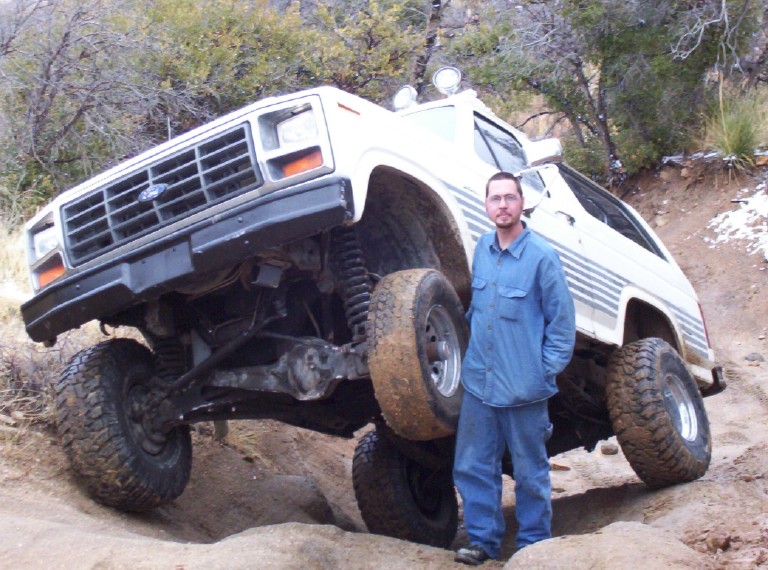 White lifted off-road SUV with a man standing next to it, showing its suspension and tires
