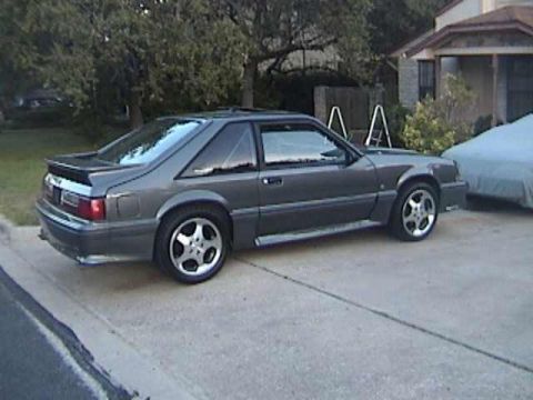 1989 Ford Mustang - A gray 1987 Ford Mustang coupe is parked on a concrete driveway next to a house.