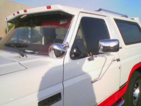 1990 Ford Bronco - White Ford Bronco with red trim and chrome mirrors is seen from a 3/4 front angle.
