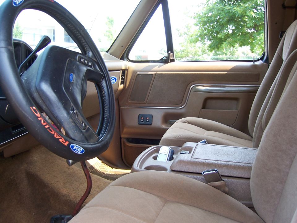 Interior shot of a truck's driver side, showing the steering wheel, dashboard, and passenger seat. Steering wheel has a 'Racing' cover