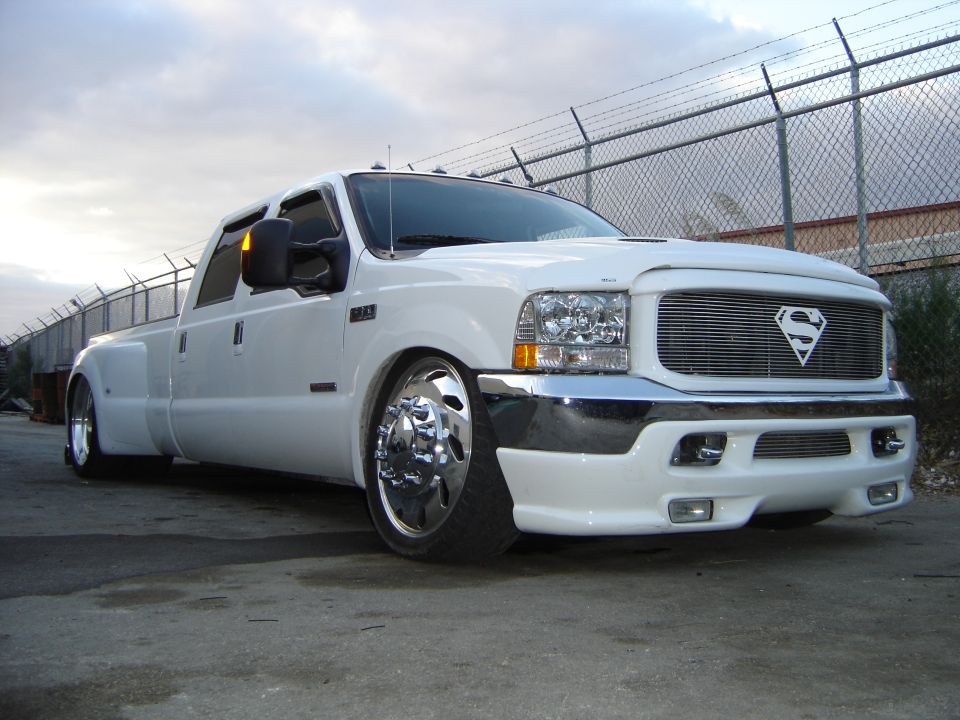 Lowered white Ford Super Duty dually pickup with chrome wheels and Superman grille emblem, front three-quarter view