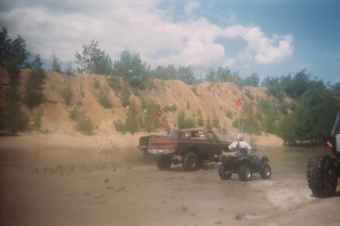 2004 Honda TRX 450 FM - An ATV and a pickup truck are on a sandy track with hills and trees in the background.