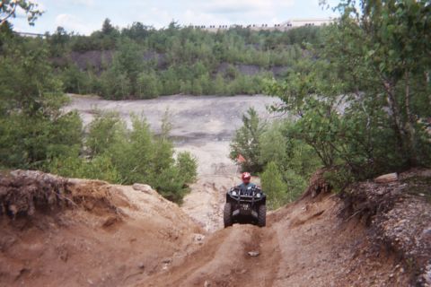 2004 Honda TRX 450 FM - An all-terrain vehicle navigates a steep, dusty trail surrounded by trees and rocky terrain.