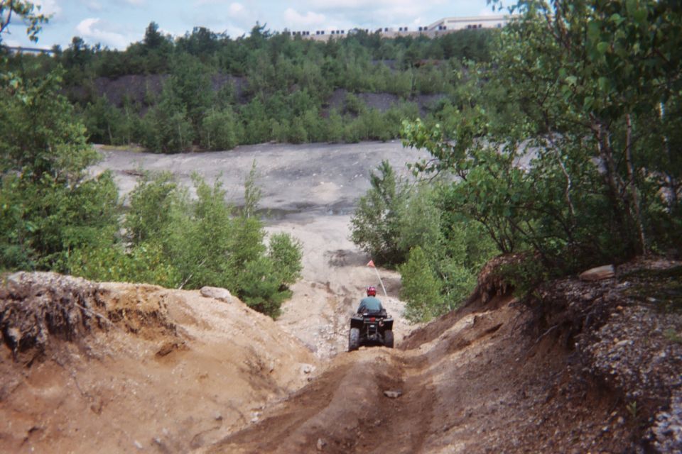 Person riding an ATV down a steep dirt path in a wooded, quarry-like area