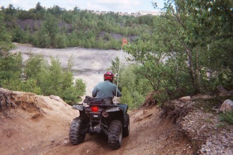 2004 Honda TRX 450 FM - An ATV navigates a rough, off-road trail with trees and a quarry in the background.