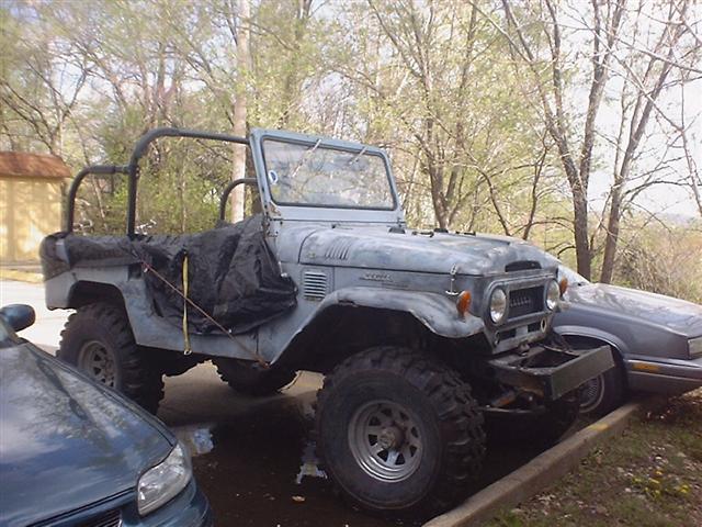 Gray Toyota Land Cruiser FJ40 with a black tarp covering part of the rear, parked next to a dark sedan
