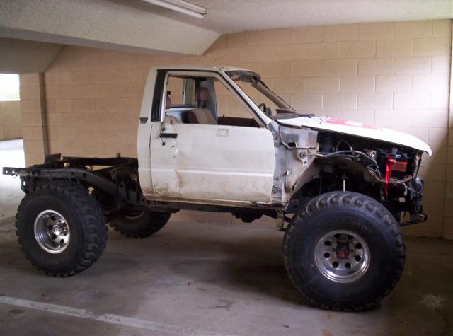 White pickup truck chassis with large tires, missing front body panels and engine components