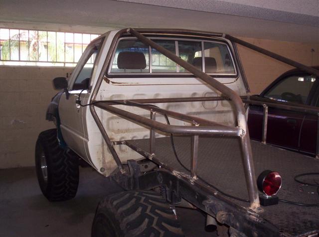 Pickup truck with custom roll cage and large tires, parked next to another vehicle