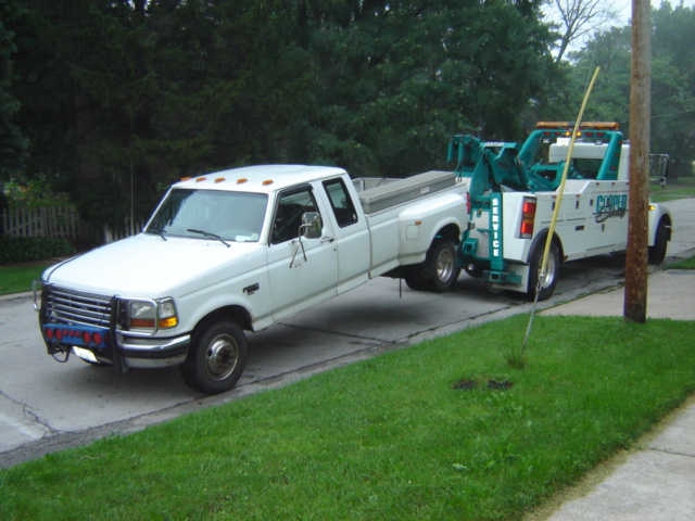 1992 Ford Bronco being towed by a white tow truck, front grille visible