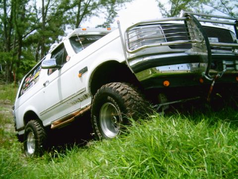 1995 Ford Bronco - This 1995 Ford Bronco is captured in a three-quarter front view, navigating a grassy slope with its off-road tires.
