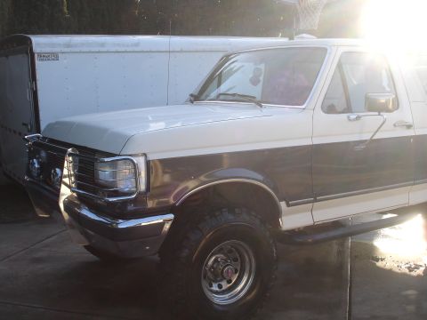 1989 Ford Bronco - This 1989 Ford Bronco is parked next to a white cargo trailer, with the sun glinting off the vehicle.