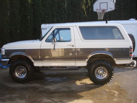 1989 Ford Bronco - This two-tone 1989 Ford Bronco features a side profile with prominent dark brown trim and raised suspension.