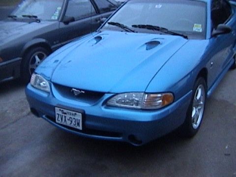 1989 Ford Mustang - A blue Ford Mustang is parked next to another vehicle. The Mustang has a prominent hood scoop.