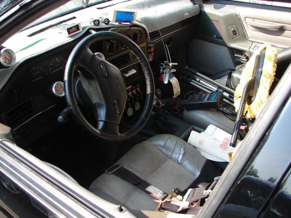 Worn car interior with steering wheel, aftermarket gauges and gear shift, gray cloth seats