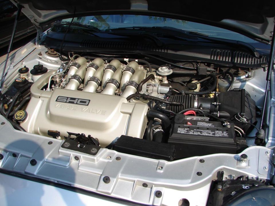 Ford SHO V6 engine with "SHO 3.0L 24 VALVE" cover. Battery and air intake visible