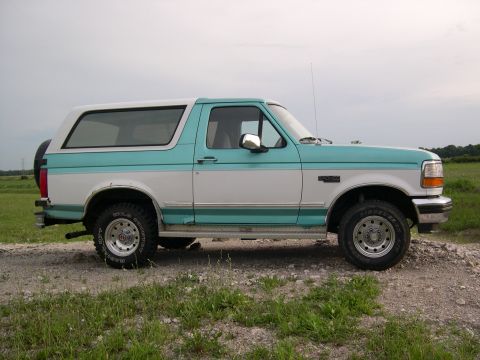 1994 Ford Bronco - This two-tone Ford Bronco is shown from the side, parked on a gravelly area with grass.