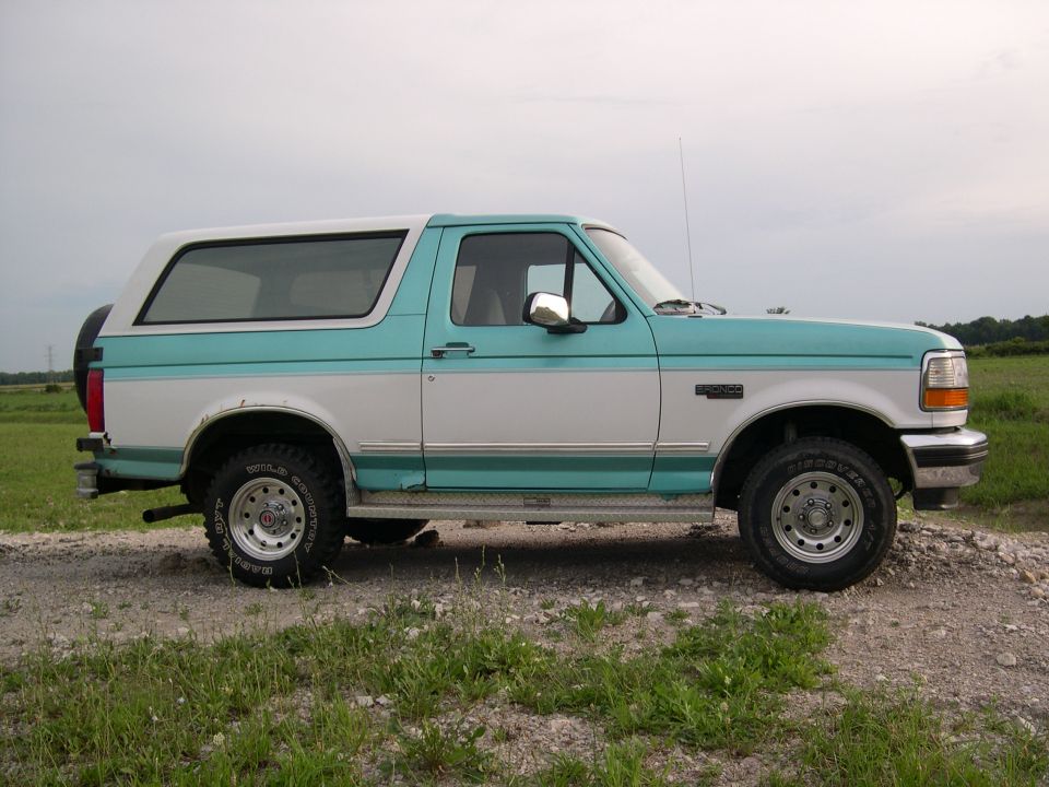 Teal and white Ford Bronco SUV in side view parked on gravel