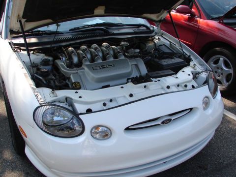 1992 Ford Taurus - The engine bay of a white 1992 Ford Taurus SHO, with the hood open, revealing the V8 engine.