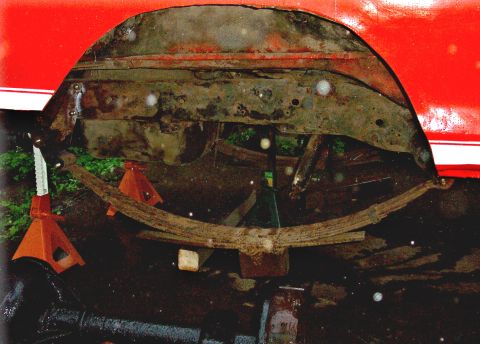 1978 Ford Bronco - The vehicle's undercarriage is visible, supported by jack stands, with heavily rusted leaf springs.