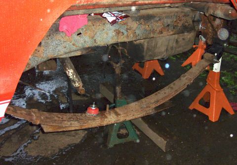 1978 Ford Bronco - The undercarriage of a red vehicle is supported by jack stands, revealing extensive rust and a fuel tank.