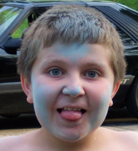 1978 Ford Bronco - A child with face paint sticks their tongue out in front of a black car.