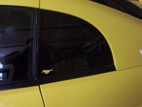 2002 Ford Mustang - Side view of a yellow 2002 Ford Mustang, showing the quarter panel and window trim with emblem.