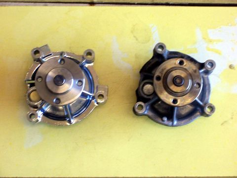 2002 Ford Mustang - Comparison of a new and used car water pump, both with a central pulley mechanism and mounting holes.