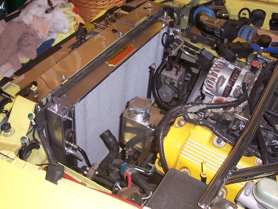 Engine bay with a large aluminum radiator, yellow valve covers, and an alternator. Some hoses and wiring are visible