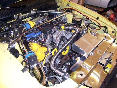 2002 Ford Mustang - The engine bay of a yellow 2002 Ford Mustang shows custom modifications including chrome intake piping and a polished coolant reservoir.
