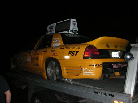 1992 Ford Crown Victoria - Modified yellow taxi with racing decals and a spoiler is loaded onto a flatbed truck.