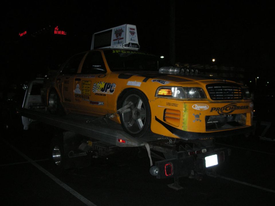 Yellow JPC Racing ProCharger-sponsored Ford sedan on a flatbed tow truck at night