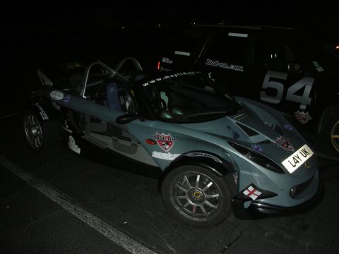 1992 Ford Crown Victoria - A Lotus Elise is parked next to a black SUV with racing decals and the number 54.
