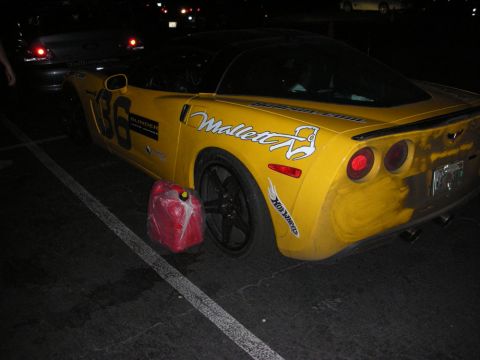 1992 Ford Crown Victoria - A yellow sports car with racing decals is parked with a red gas can by its rear tire.