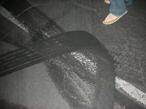 1992 Ford Crown Victoria - Tire marks on a paved surface, with a person's legs and feet visible in the upper right corner.