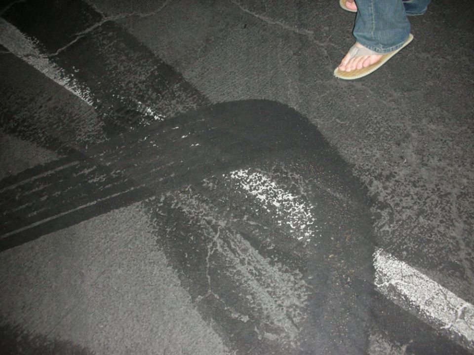 Tire marks on asphalt with a person's feet in flip-flops and jeans visible at the top right