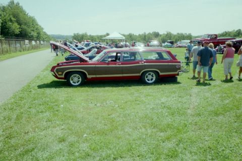 1970 Ford Ranchero - A two-tone station wagon is displayed at an outdoor car show with other vehicles and people in the background.