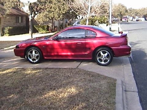 1989 Ford Mustang - A red coupe is parked on the side of the road in front of a house.