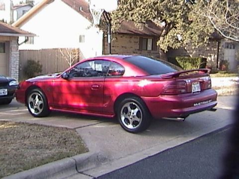 1989 Ford Mustang - A red coupe with a spoiler is parked on a driveway next to a house.