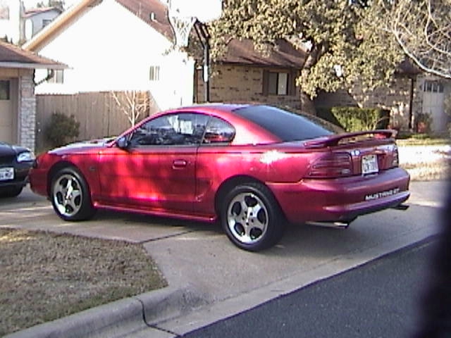 Red coupe parked on driveway, rear quarter view. "MUSTANG GT" text visible on rear bumper