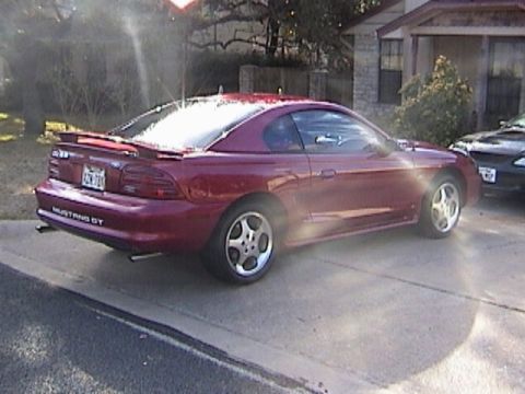 1989 Ford Mustang - This red 1994 Ford Mustang GT is parked in a driveway next to another vehicle.