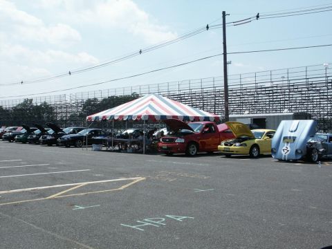 2001 Mercury Grand Marquis - Outdoor car show with multiple vehicles displayed under a large tent and in an open lot.