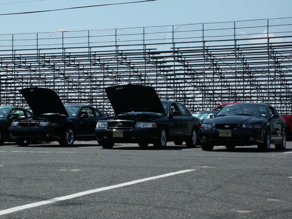 Four black cars parked in a lot, three with hoods up. The front car is a 2001 Mercury Grand Marquis
