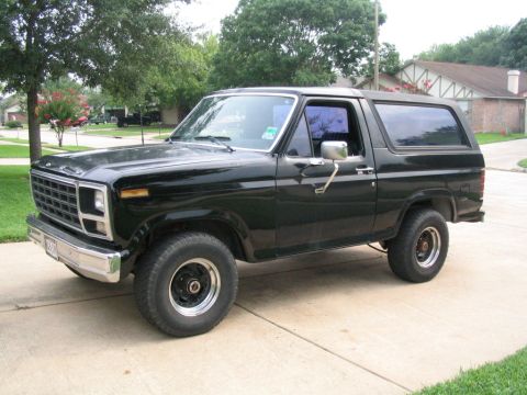 1983 Ford Bronco - This black Ford Bronco from the early 1980s is parked on a suburban driveway.