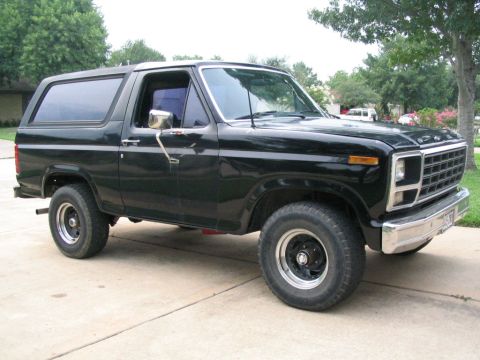 1983 Ford Bronco - This black Ford Bronco is parked outside on a paved surface with trees visible behind it.