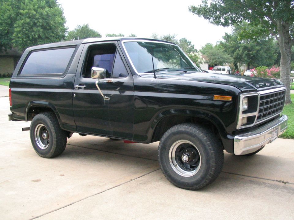 Black Ford Bronco parked on concrete driveway, trees in background