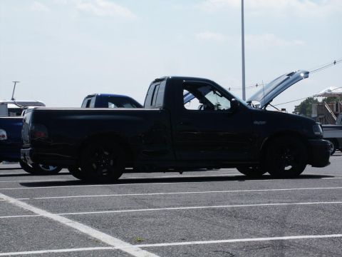 2001 Mercury Grand Marquis - A black Ford F-150 Lightning pickup truck is parked in a lot with its hood up, alongside other vehicles under a bright sky.