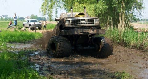 1978 Ford Bronco - A heavily modified truck navigates a muddy obstacle course, while another truck observes from the grassy bank.