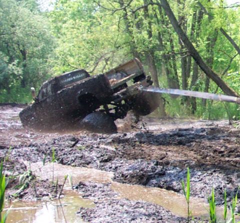 1978 Ford Bronco - A mud-caked 4x4 climbs steeply out of a rutted mud trench at a hard angle, front wheels lifted and undercarriage exposed as mud flies from…