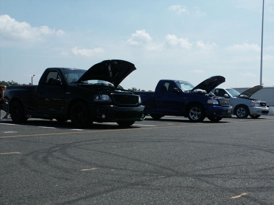 Black, blue, and silver pickup trucks parked with hoods open, plus a silver sedan